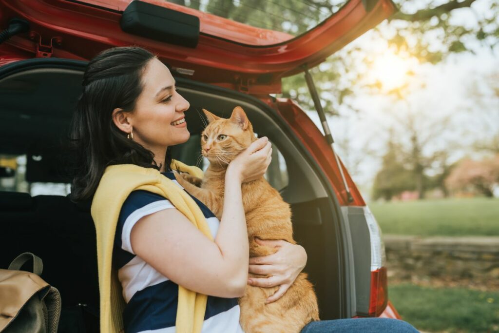 Femme tenant un chat orange à l'arrière d'une voiture.