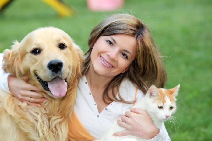 Une femme souriante avec un chien et un chat dans ses bras.