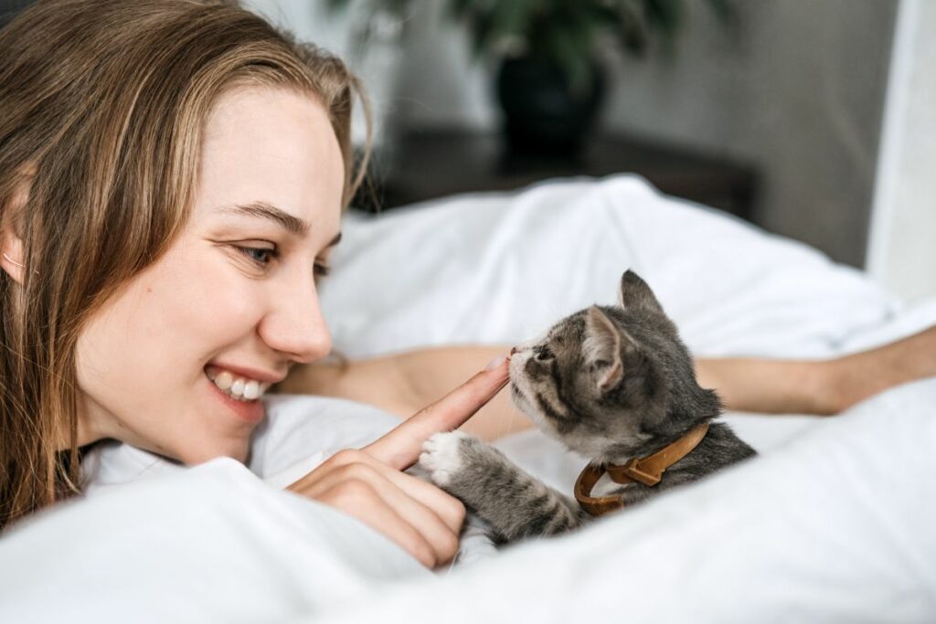 Femme souriante touchant le nez d'un chaton allongé sur un lit.